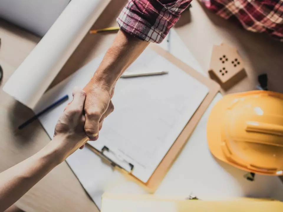 Two people shaking hands over construction paperwork
