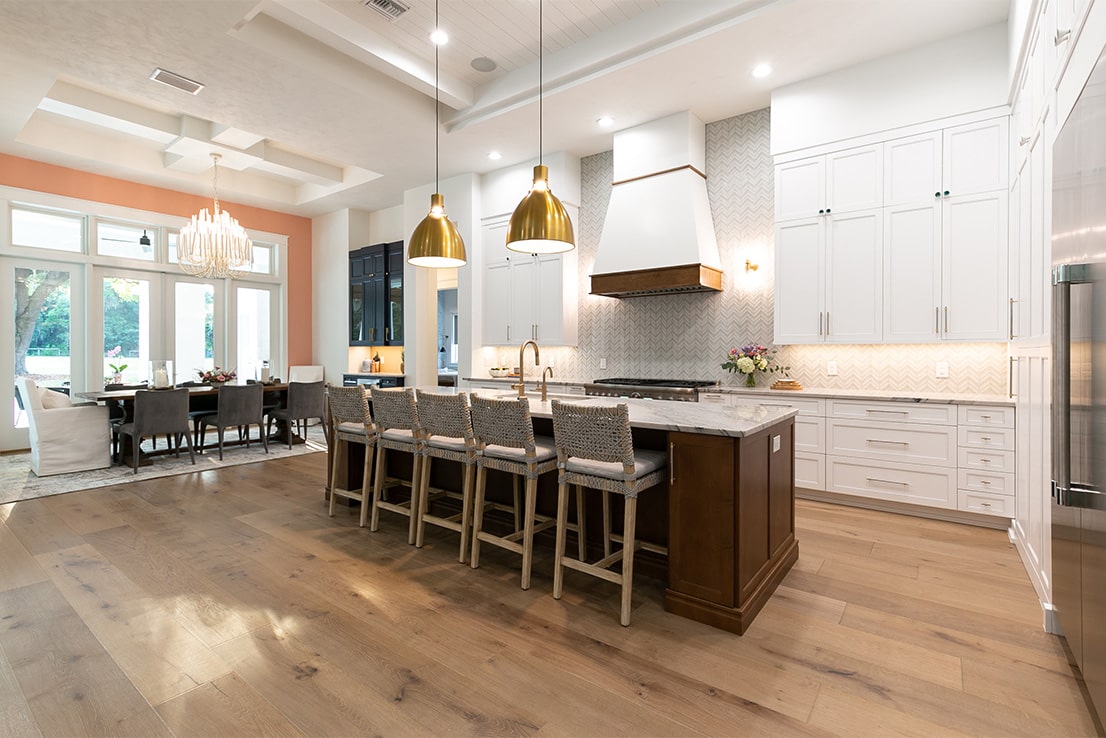 a modern white kitchen with brown island and gold pendant lighting