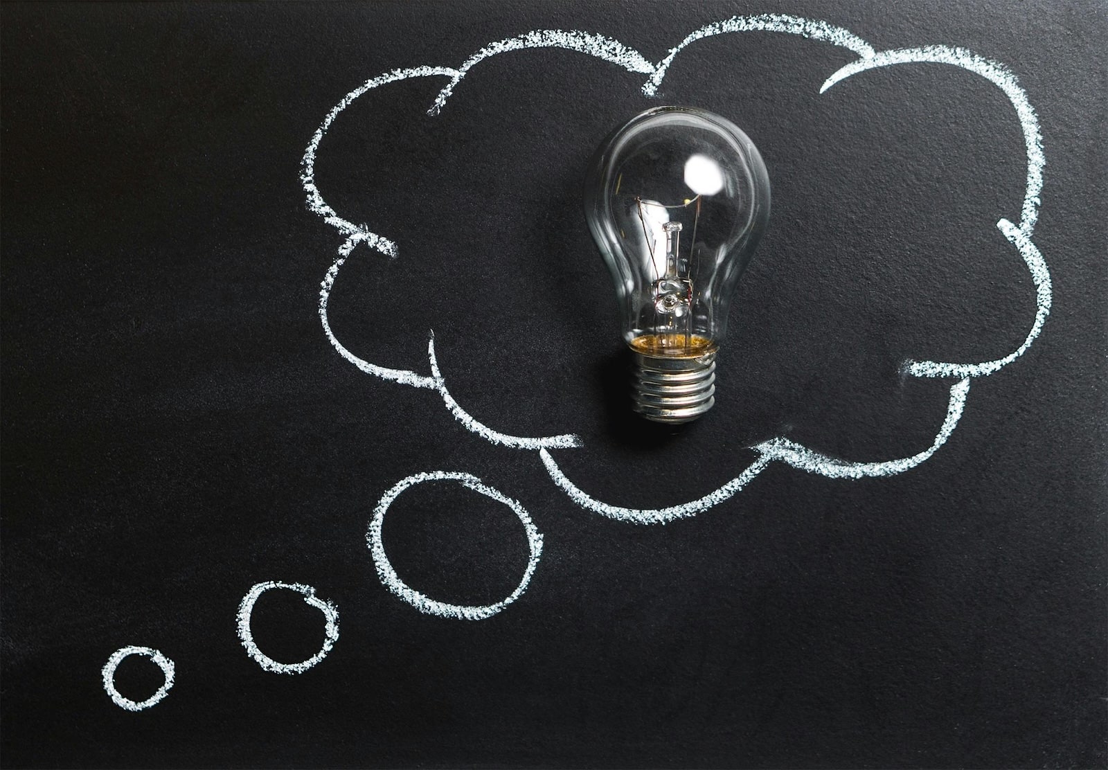 A light bulb placed on a blackboard, surrounded by a thought bubble drawn in white chalk, symbolizing an idea or creative thinking.